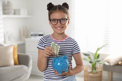 Cute girl with pocket money and piggy bank at home