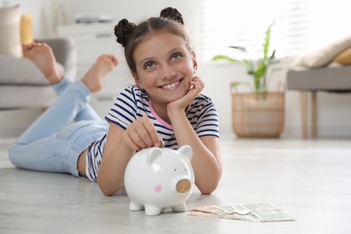 Photo of Pocket money. Cute girl putting coin into piggy bank at home, space for text