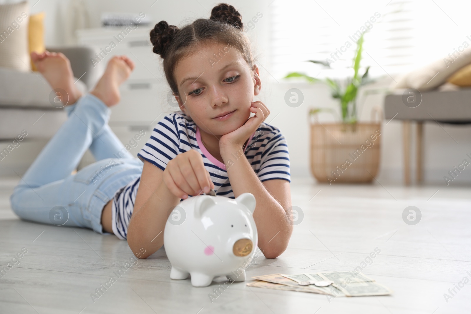 Photo of Pocket money. Cute girl putting coin into piggy bank at home, space for text