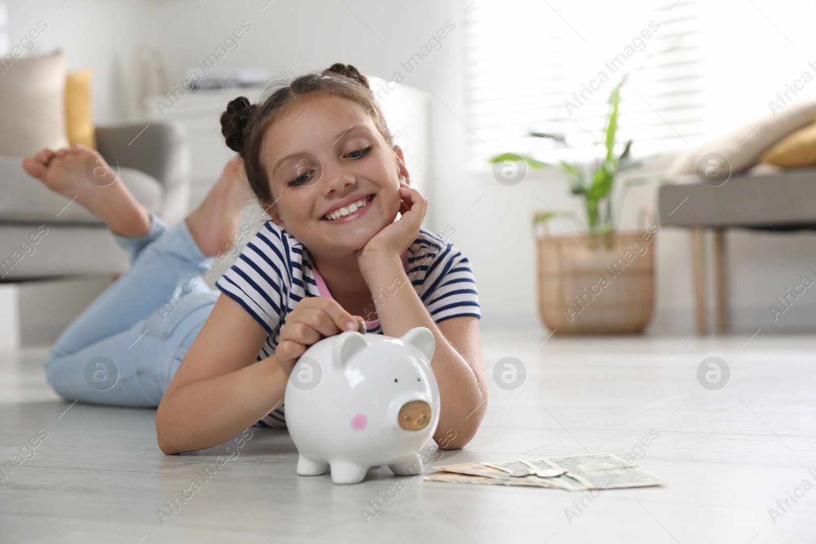 Photo of Pocket money. Cute girl putting coin into piggy bank at home, space for text