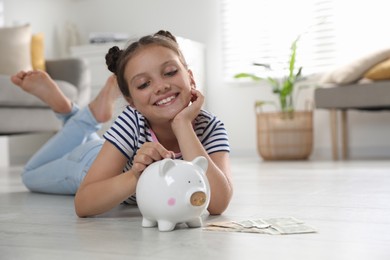 Pocket money. Cute girl putting coin into piggy bank at home, space for text