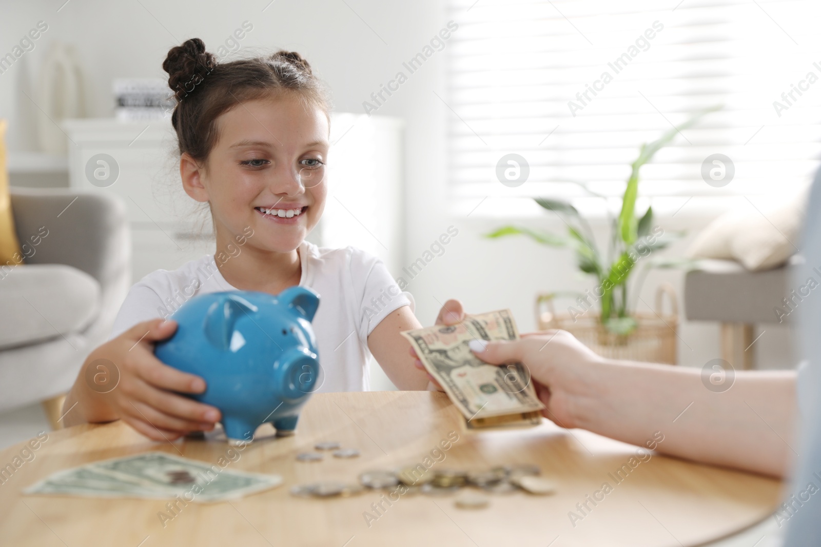 Photo of Mother giving pocket money to her daughter at table indoors