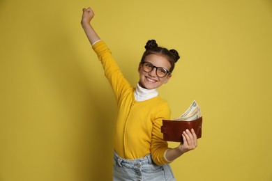 Photo of Pocket money. Cute girl with wallet and dollar banknotes on yellow background