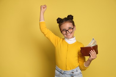 Photo of Pocket money. Cute girl with wallet and dollar banknotes on yellow background