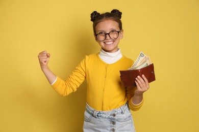 Photo of Pocket money. Cute girl with wallet and dollar banknotes on yellow background