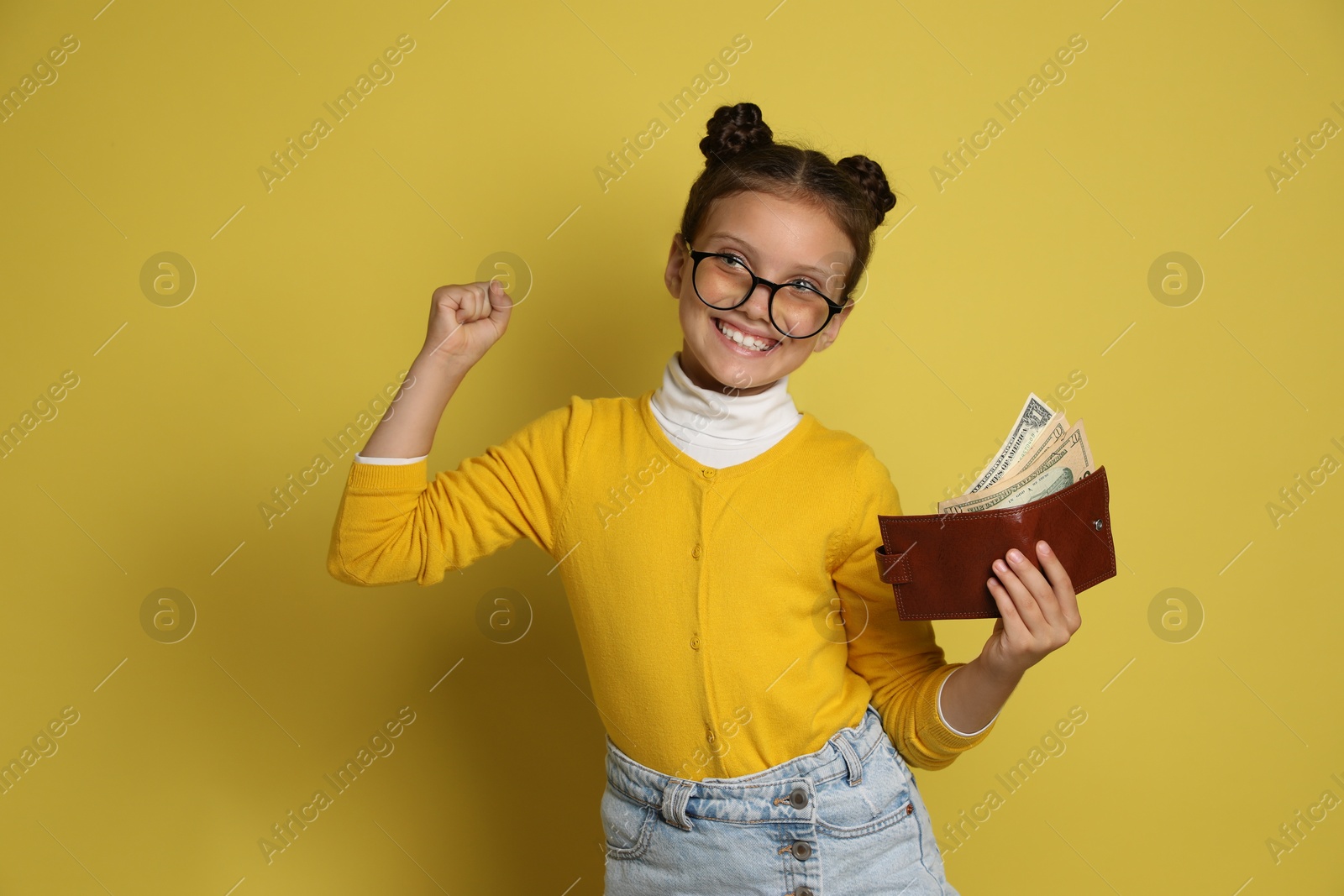 Photo of Pocket money. Cute girl with wallet and dollar banknotes on yellow background