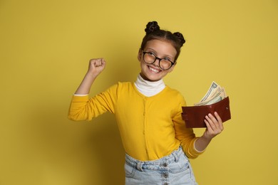 Photo of Pocket money. Cute girl with wallet and dollar banknotes on yellow background