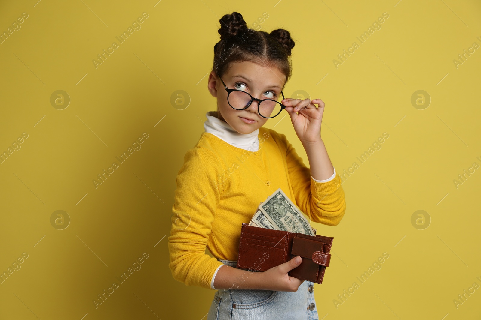 Photo of Pocket money. Cute girl with wallet and dollar banknotes on yellow background