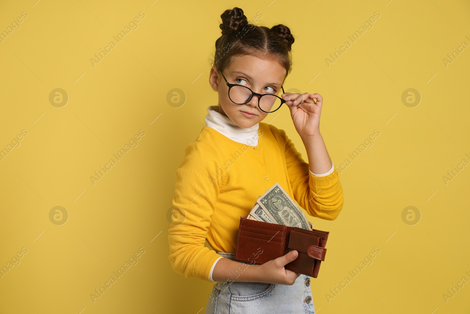 Photo of Pocket money. Cute girl with wallet and dollar banknotes on yellow background