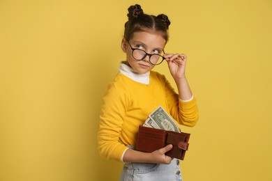 Pocket money. Cute girl with wallet and dollar banknotes on yellow background