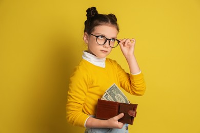 Photo of Pocket money. Cute girl with wallet and dollar banknotes on yellow background