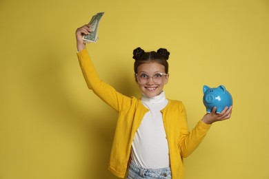 Photo of Pocket money. Cute girl with piggy bank and dollar banknotes on yellow background