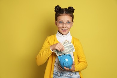 Photo of Pocket money. Cute girl with piggy bank and dollar banknotes on yellow background