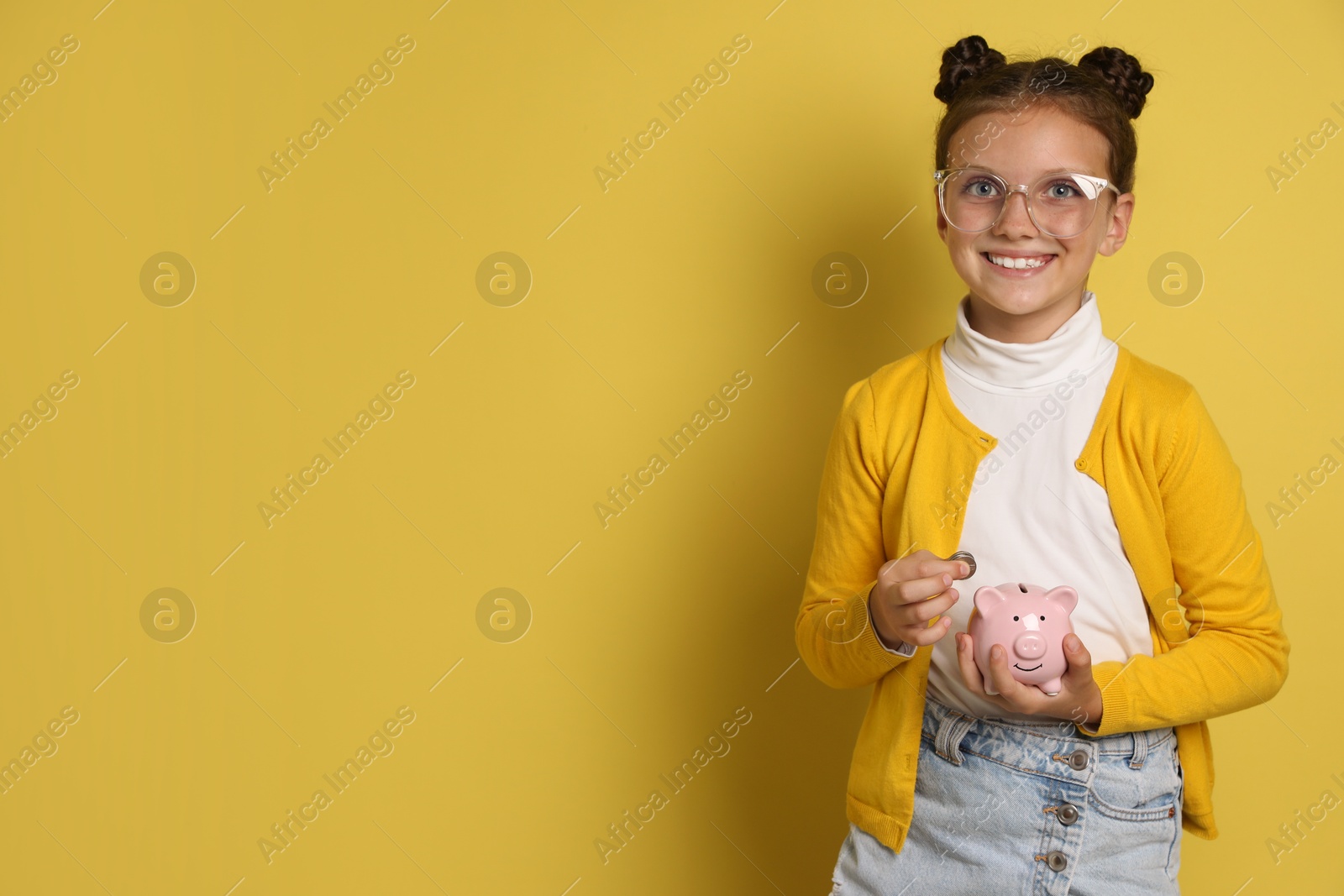 Photo of Pocket money. Cute girl with coins and piggy bank on yellow background, space for text