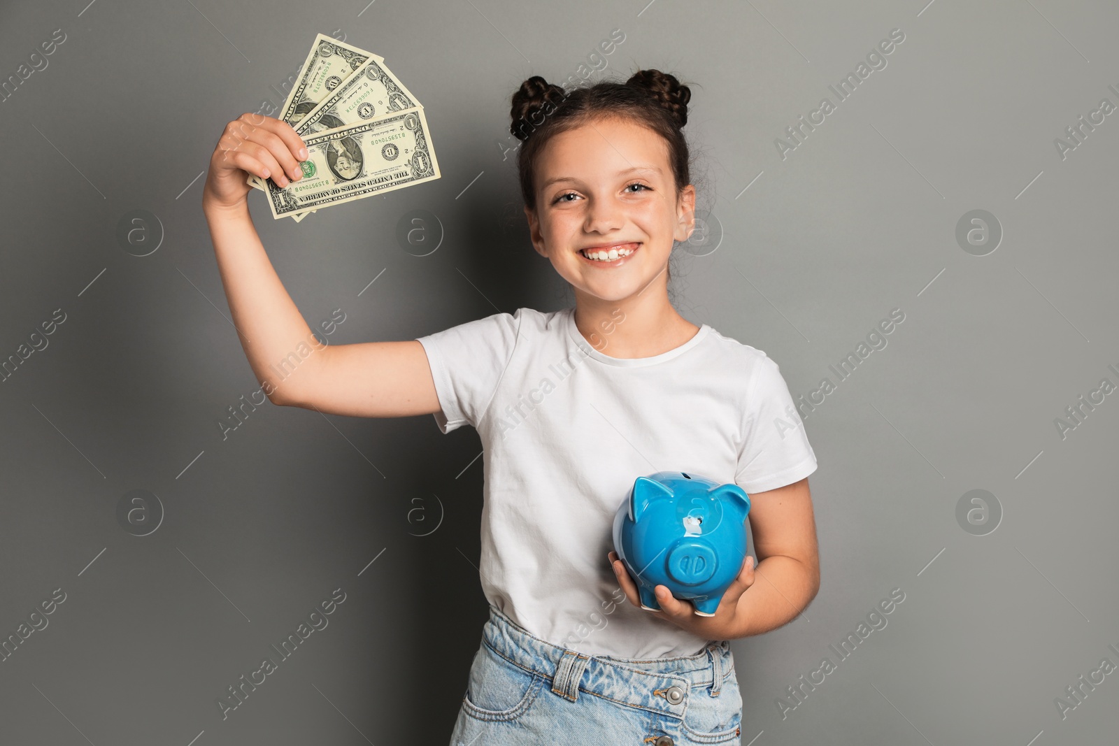 Photo of Pocket money. Cute girl with piggy bank and dollar banknotes on grey background