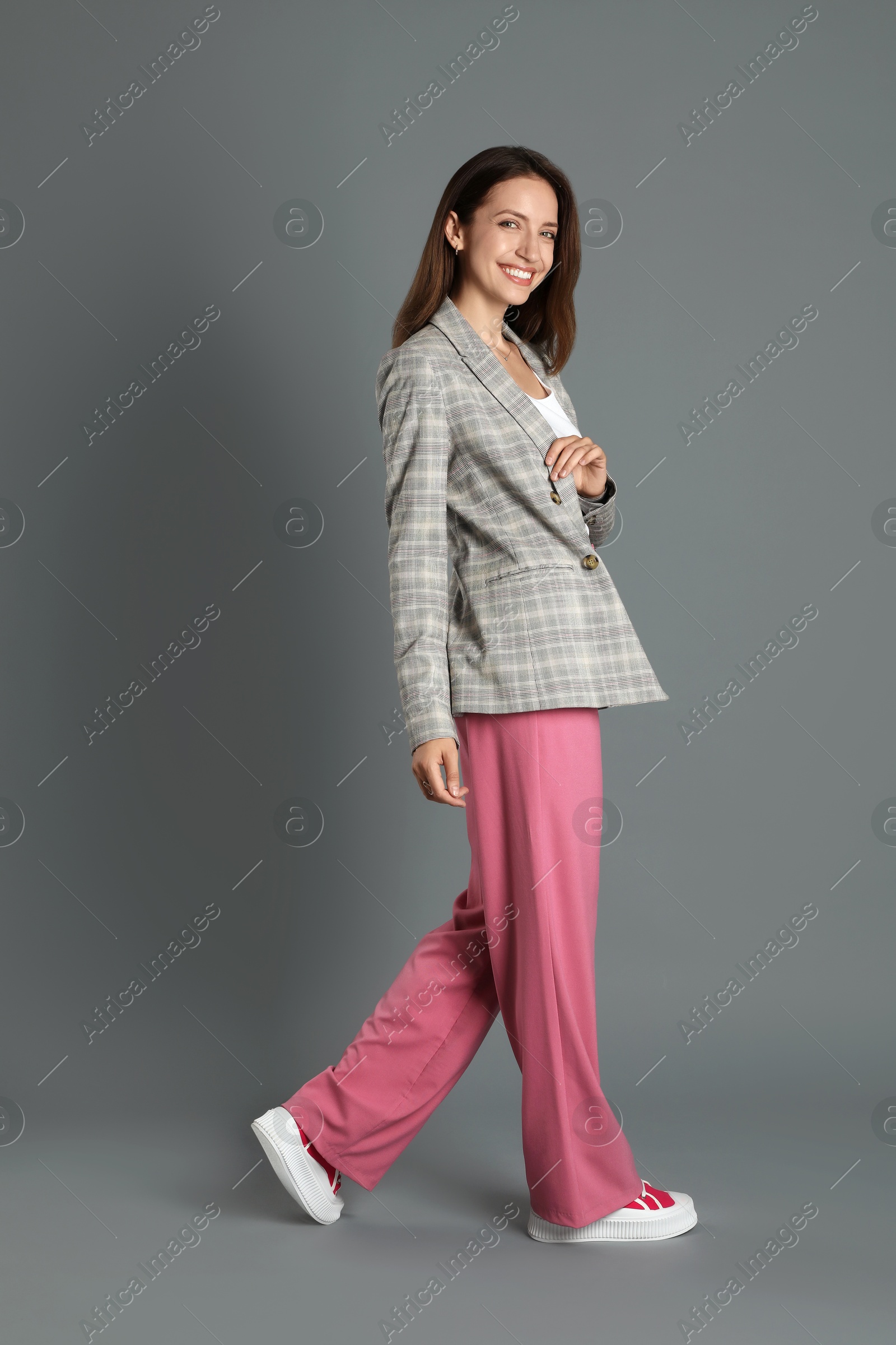 Photo of Beautiful woman in stylish jacket and pink pants on grey background