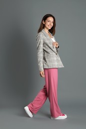 Beautiful woman in stylish jacket and pink pants on grey background