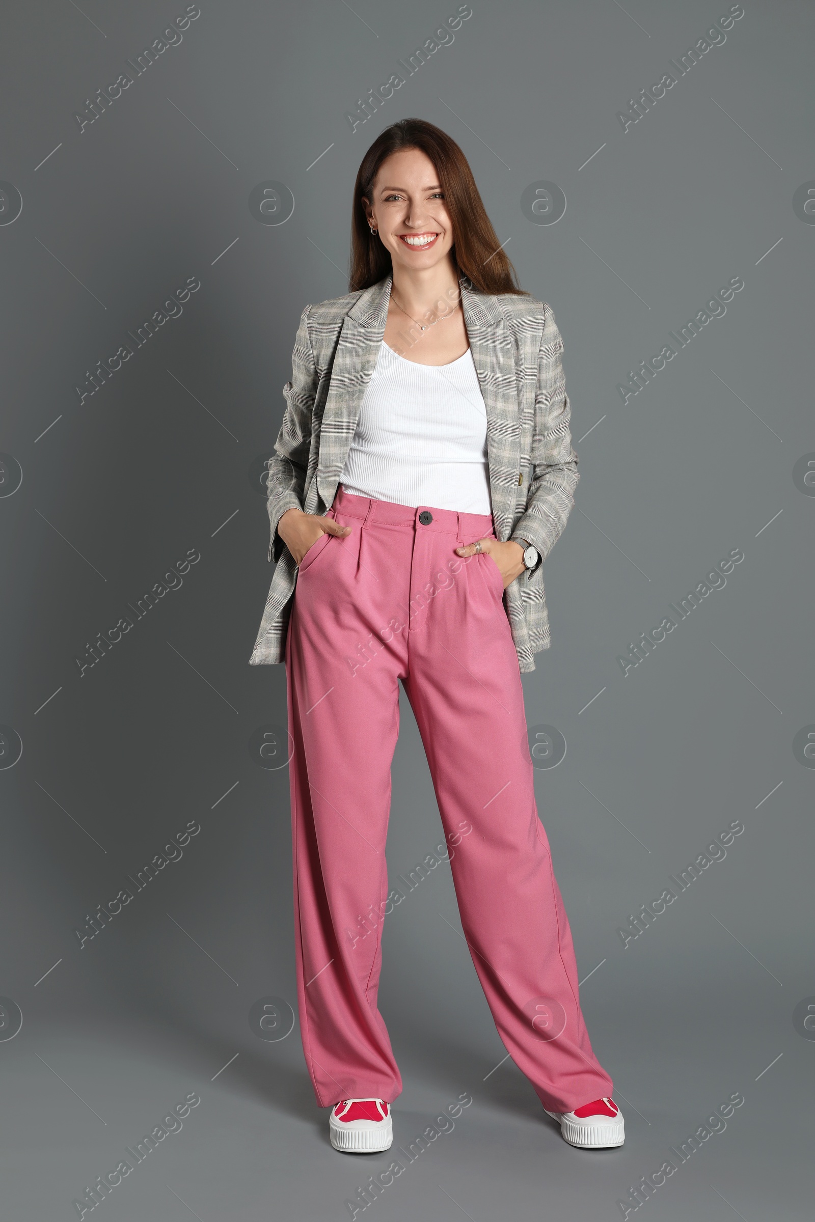 Photo of Beautiful woman in stylish jacket and pink pants on grey background