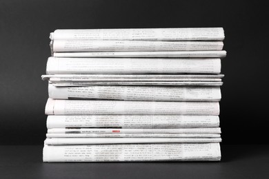 Stack of newspapers in different languages on black background