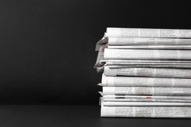 Stack of newspapers in different languages on black background. Space for text