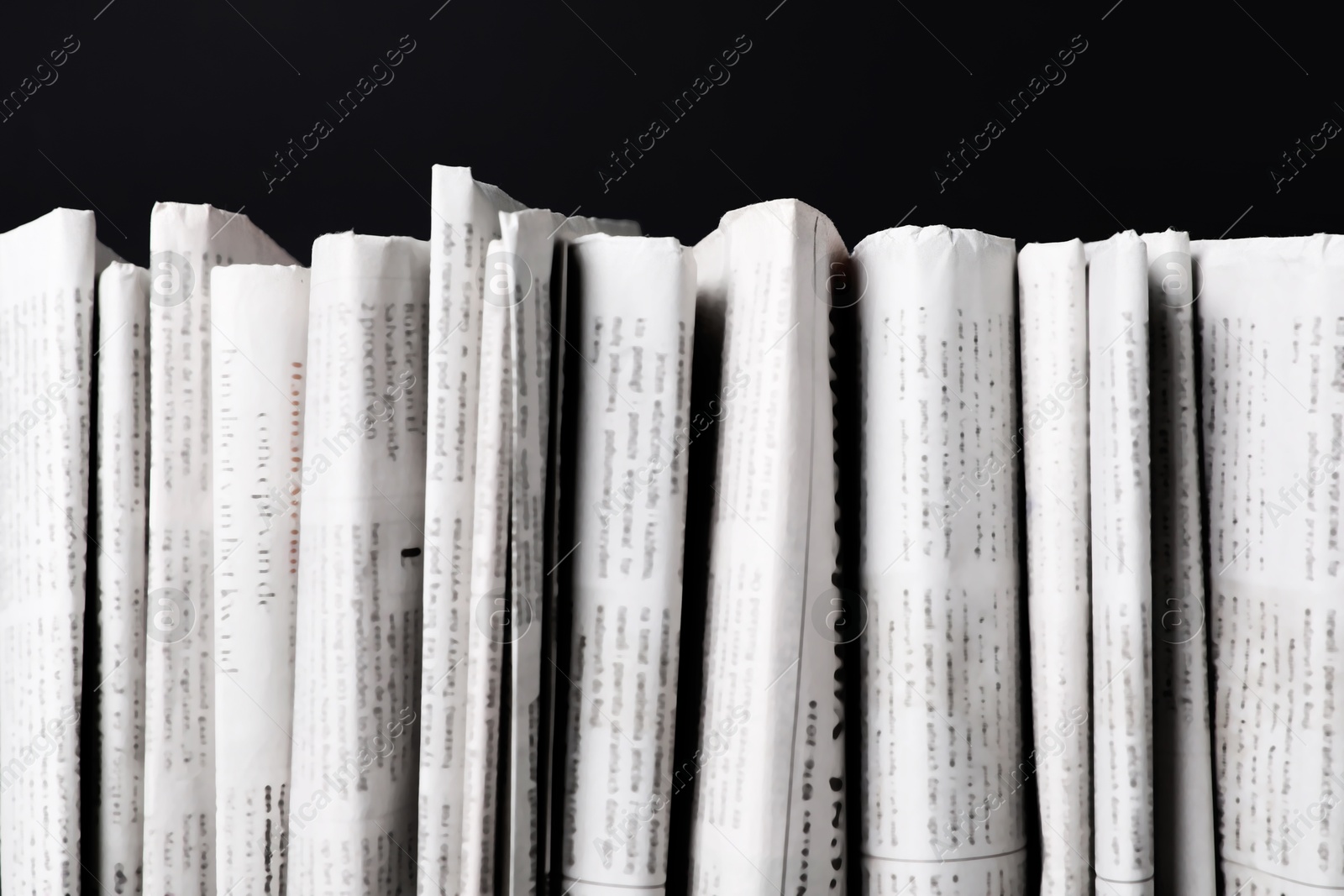 Photo of Many newspapers in different languages on black background, closeup