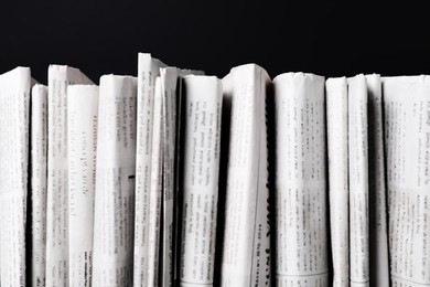 Photo of Many newspapers in different languages on black background, closeup