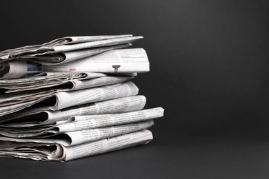 Stack of newspapers in different languages on black background. Space for text