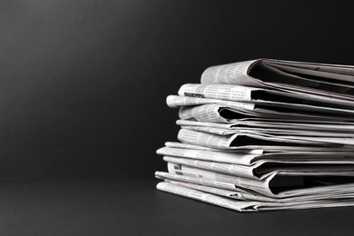 Stack of newspapers in different languages on black background. Space for text