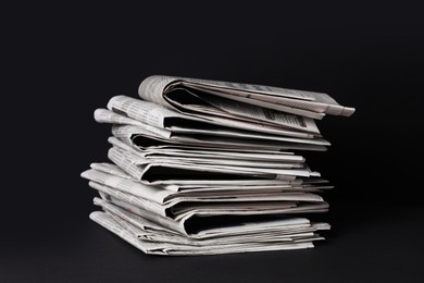 Stack of newspapers in different languages on black background