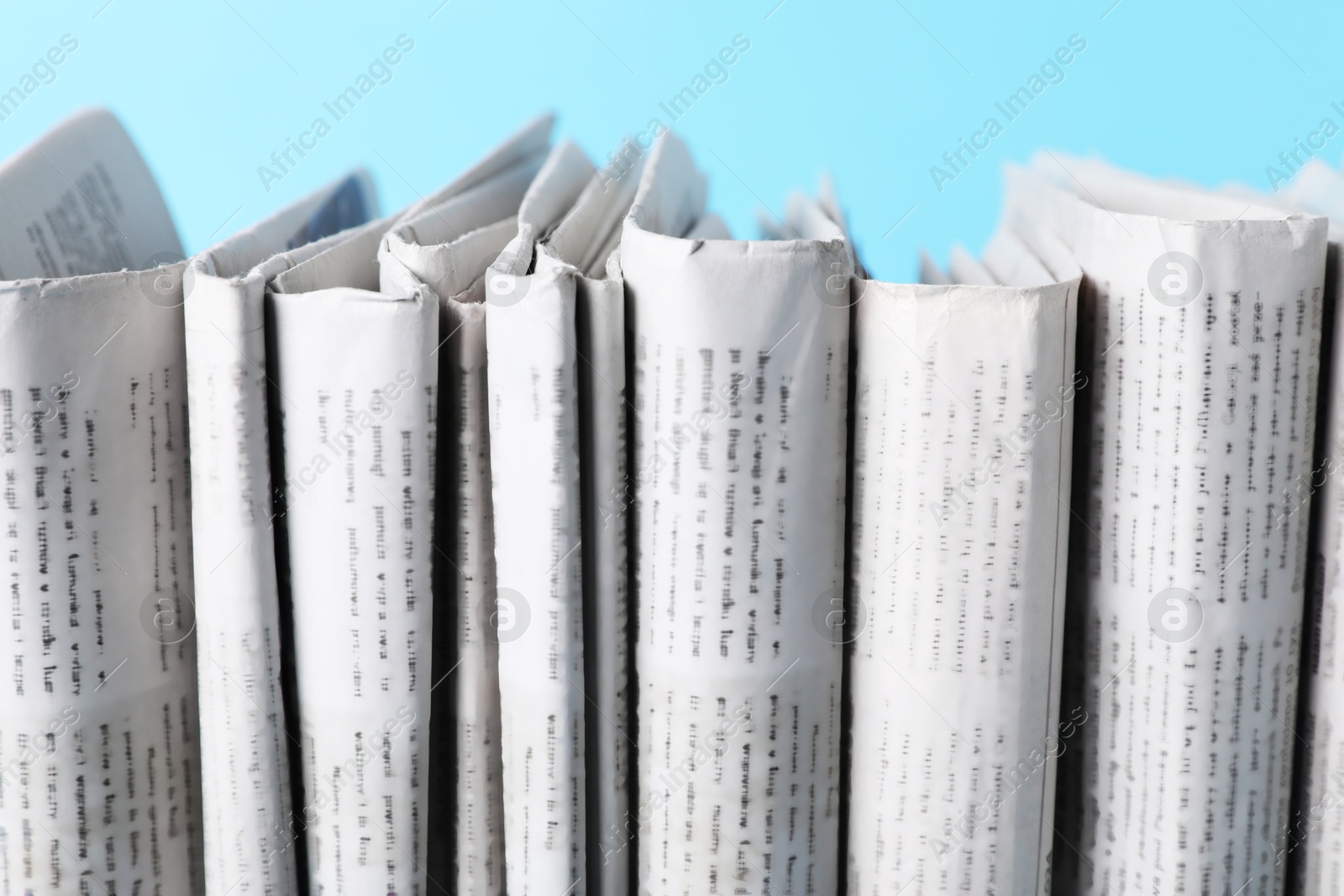 Photo of Many newspapers in different languages on light blue background, closeup