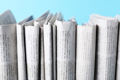 Photo of Many newspapers in different languages on light blue background, closeup