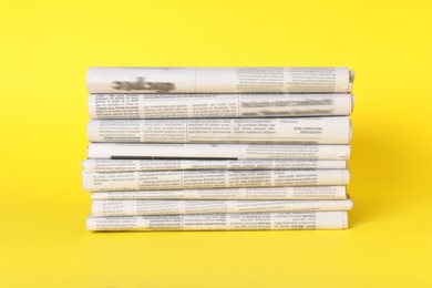 Stack of many newspapers in different languages on yellow background