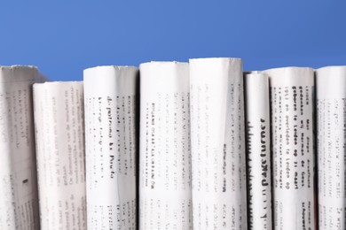 Many newspapers in different languages on blue background, closeup