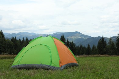 Photo of Tent on green grass in mountains. Camping equipment