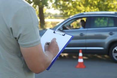 Examiner with clipboard during exam at driving school test track, closeup