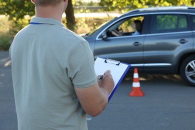 Examiner with clipboard during exam at driving school test track, closeup