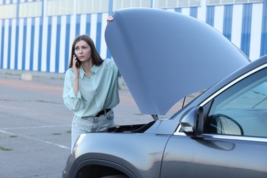 Stressed woman talking on phone near broken car outdoors