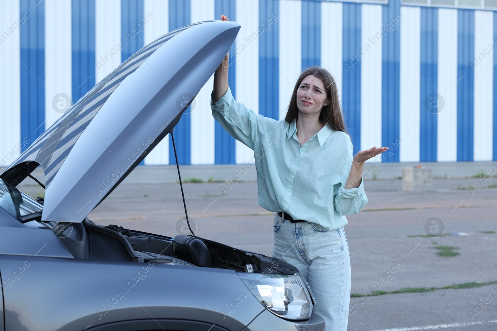 Photo of Stressed woman standing near broken car outdoors