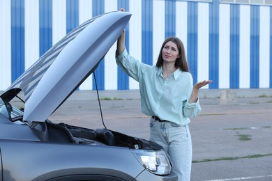 Stressed woman standing near broken car outdoors