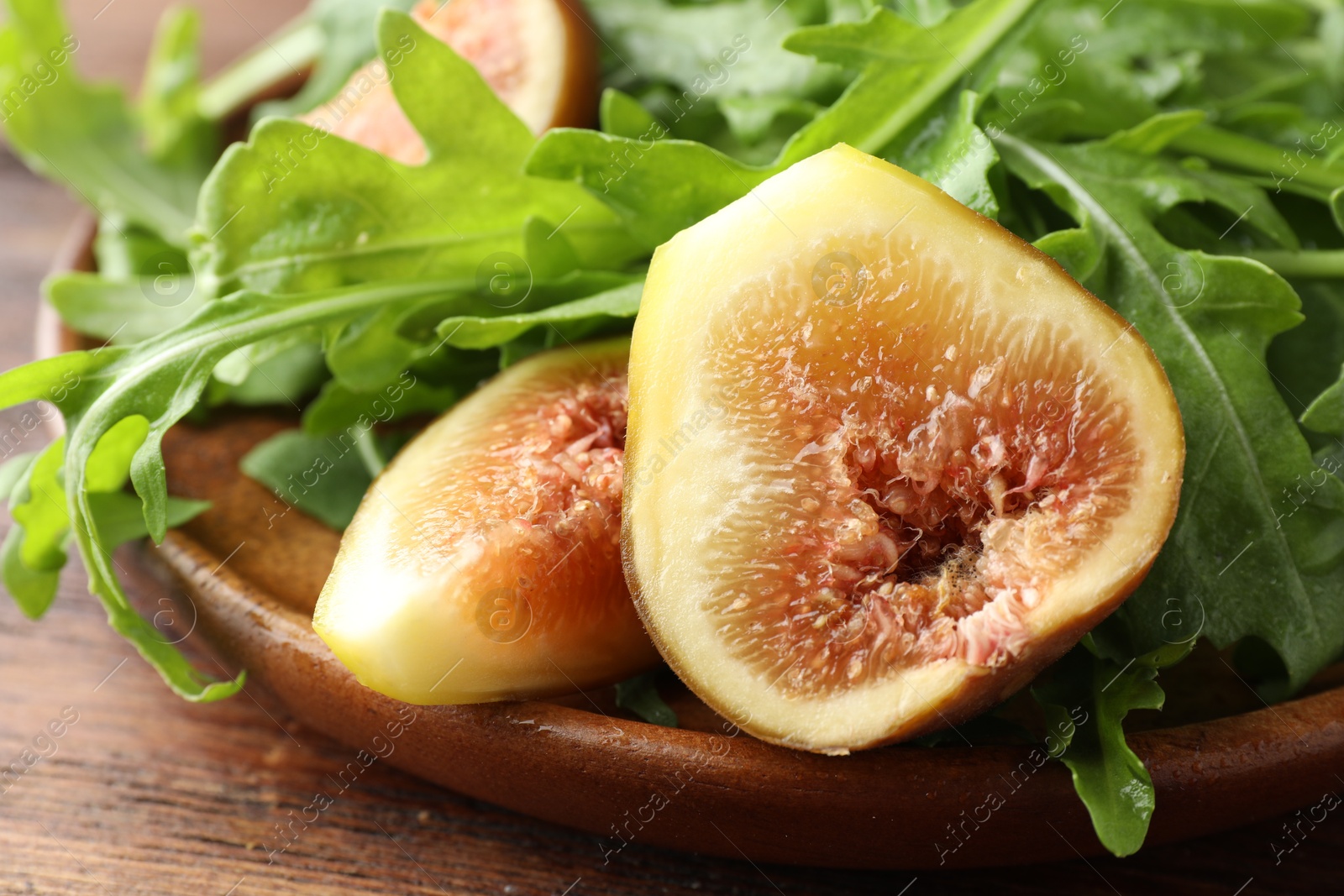 Photo of Fresh arugula and cut fig on wooden table, closeup