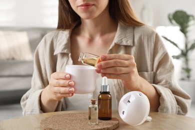 Woman adding essential oil to aroma diffuser at home, closeup