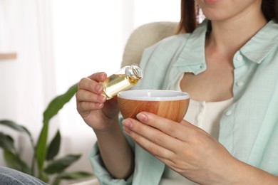 Photo of Woman adding essential oil to aroma diffuser at home, closeup