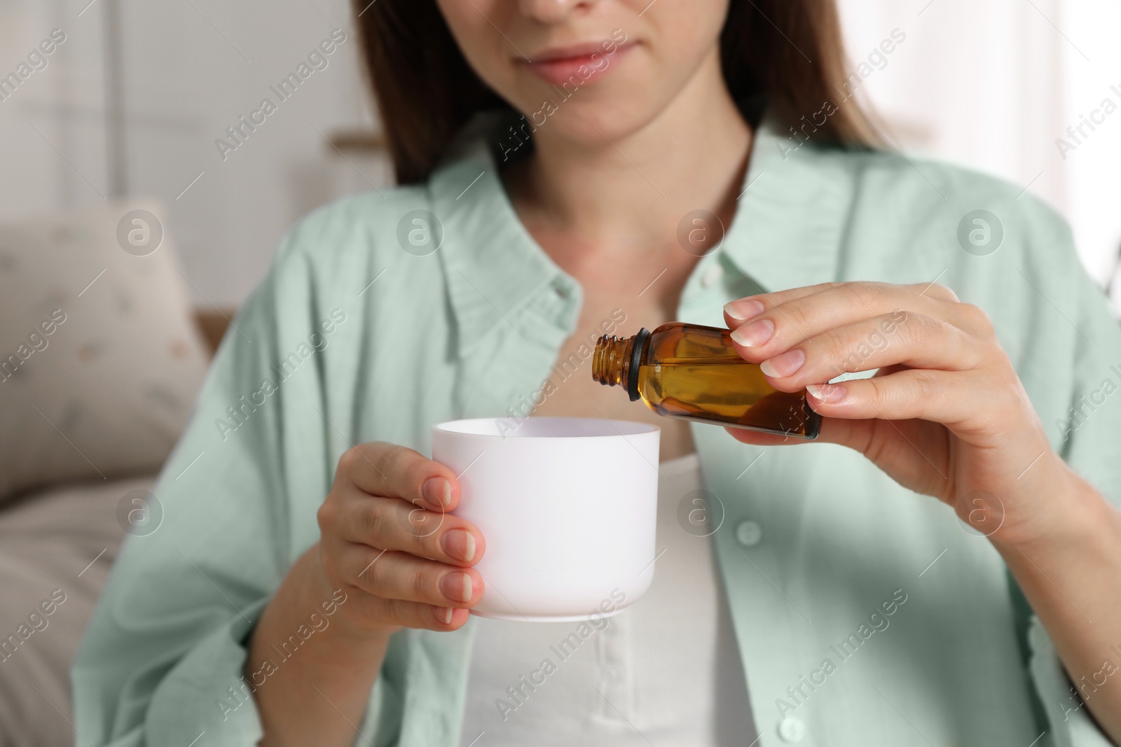 Photo of Woman adding essential oil to aroma diffuser at home, closeup