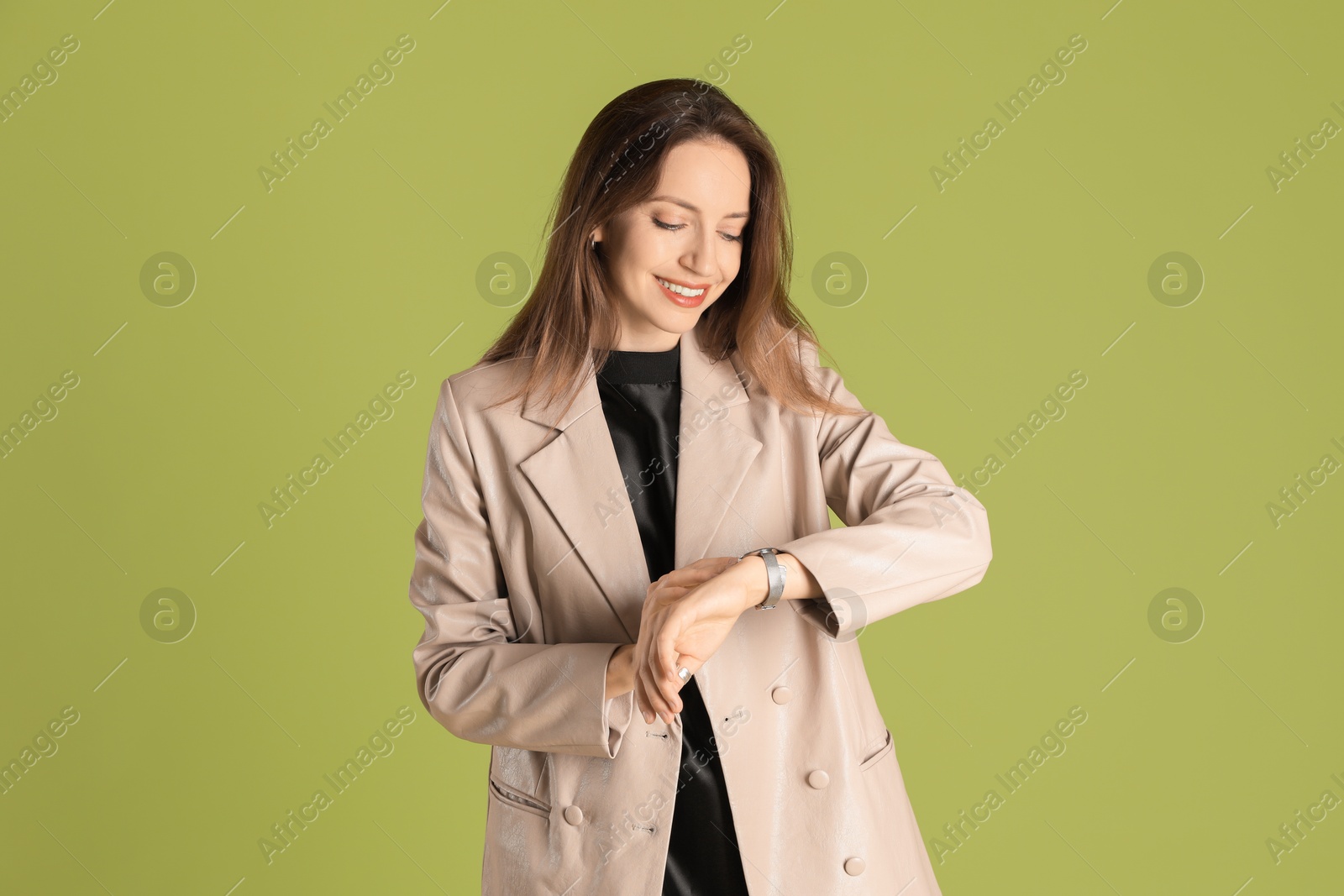 Photo of Beautiful woman in stylish beige jacket checking time on olive background