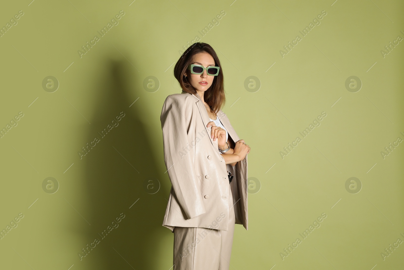 Photo of Beautiful woman in stylish beige suit and sunglasses on olive background