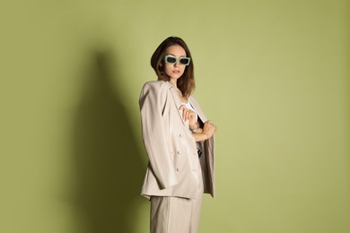 Beautiful woman in stylish beige suit and sunglasses on olive background