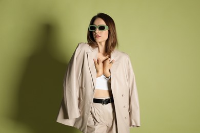 Photo of Beautiful woman in stylish beige suit and sunglasses on olive background