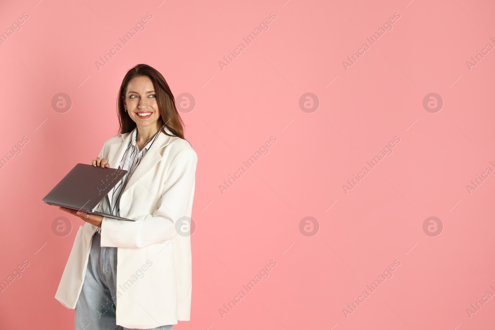 Photo of Beautiful woman in stylish white jacket with laptop on pink background, space for text