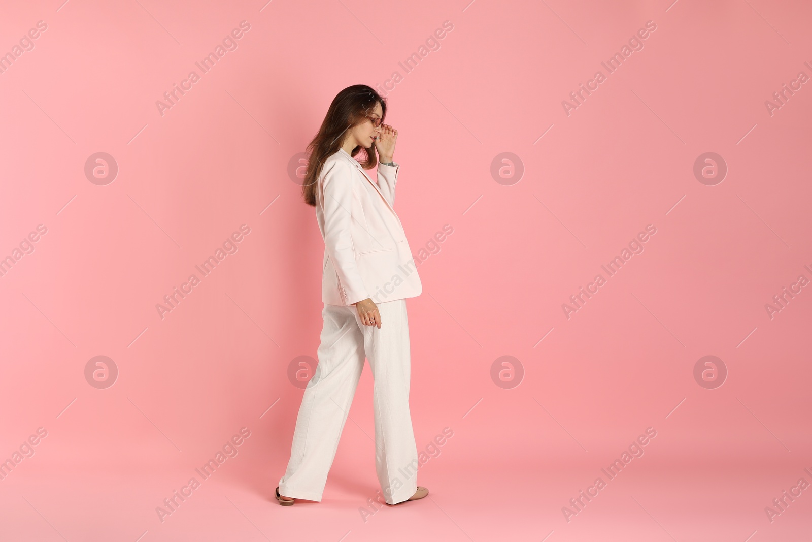 Photo of Beautiful woman in stylish white suit and sunglasses on pink background