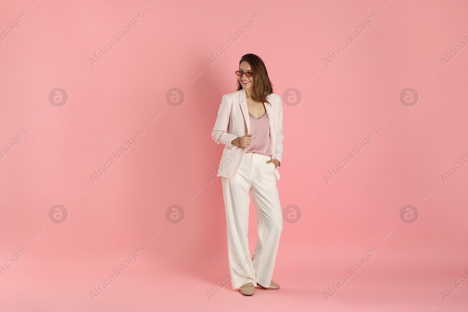 Photo of Beautiful woman in stylish white suit and sunglasses on pink background